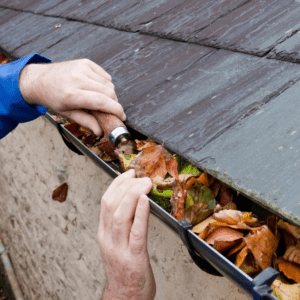 A person scraping leaves from the gutter
